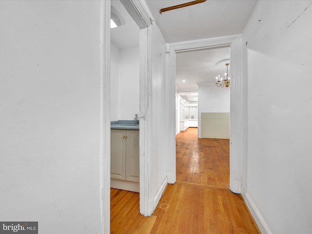 corridor featuring light hardwood / wood-style flooring, an inviting chandelier, and sink