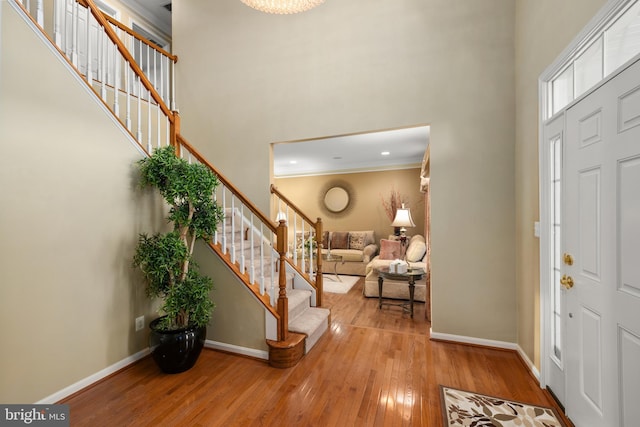 entryway with light hardwood / wood-style floors, a towering ceiling, and crown molding