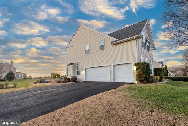 property exterior at dusk featuring a lawn and a garage