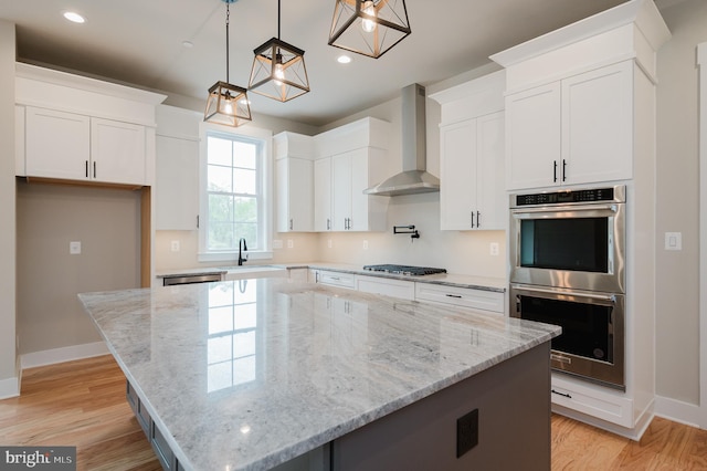 kitchen with white cabinets, stainless steel appliances, wall chimney exhaust hood, and a kitchen island