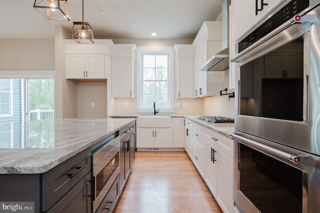 kitchen with stainless steel appliances, light stone counters, light hardwood / wood-style floors, white cabinets, and decorative light fixtures