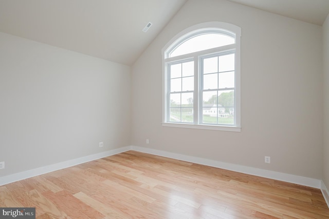 spare room with lofted ceiling, a wealth of natural light, and light hardwood / wood-style floors