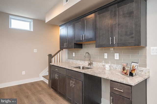 kitchen featuring sink, light stone counters, and dark brown cabinetry