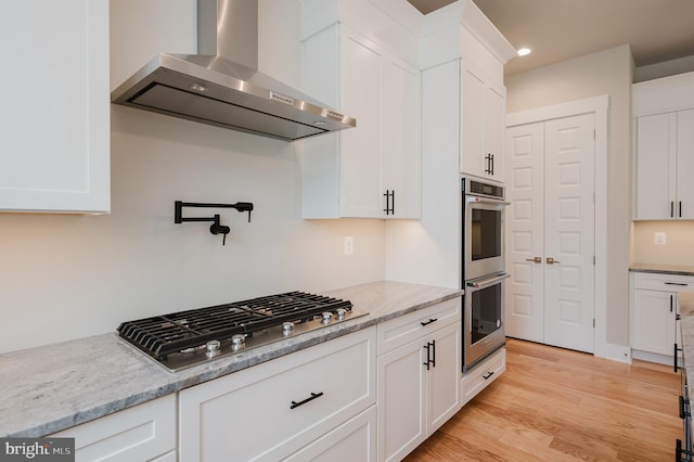 kitchen featuring stainless steel appliances, white cabinetry, and wall chimney exhaust hood