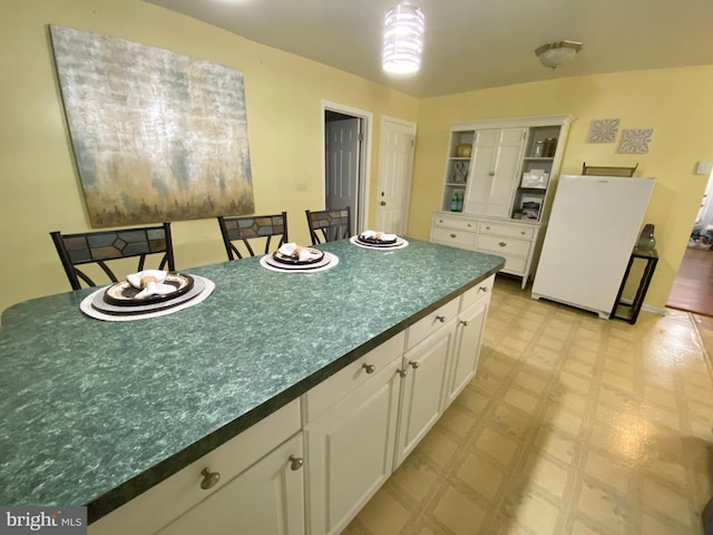 kitchen with a center island, white fridge, white cabinetry, and a breakfast bar area