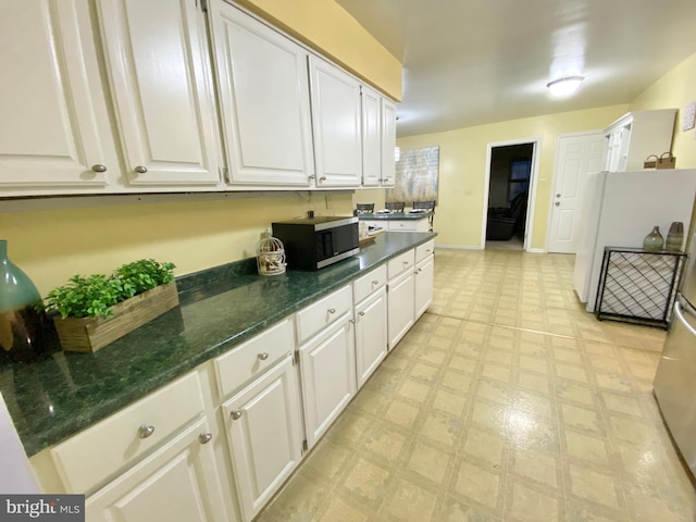 kitchen featuring white refrigerator, white cabinetry, and dark stone counters