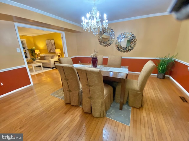 dining area with ornamental molding, a notable chandelier, and light wood-type flooring