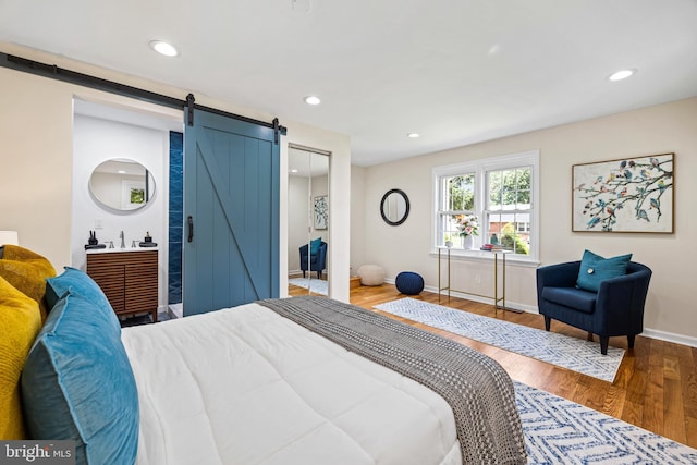 bedroom with hardwood / wood-style flooring, a barn door, connected bathroom, and a closet