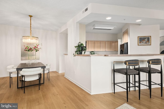 kitchen with hanging light fixtures, an inviting chandelier, black fridge, light hardwood / wood-style floors, and light brown cabinetry