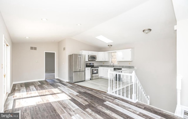 kitchen with sink, vaulted ceiling with skylight, appliances with stainless steel finishes, light hardwood / wood-style floors, and white cabinetry