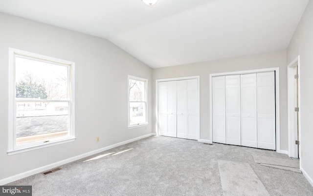 unfurnished bedroom with multiple closets, light carpet, and lofted ceiling