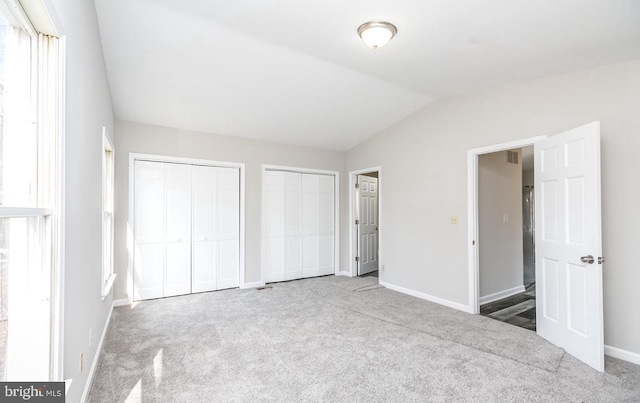 unfurnished bedroom featuring carpet, two closets, and vaulted ceiling