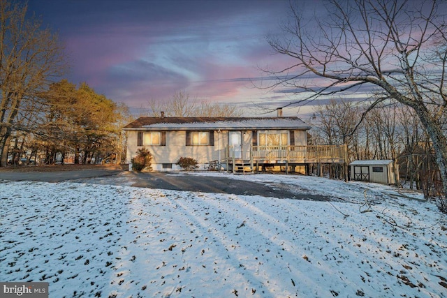 snow covered back of property with a wooden deck and a storage unit