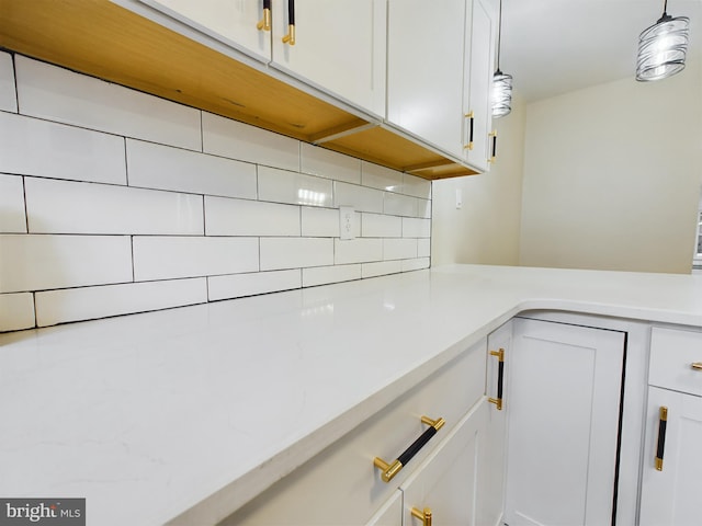 interior details featuring decorative backsplash, white cabinetry, and pendant lighting