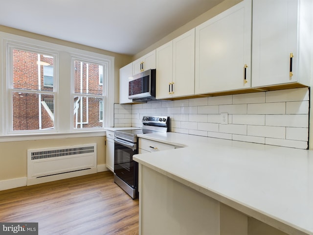 kitchen with white cabinets, light wood-type flooring, tasteful backsplash, radiator heating unit, and stainless steel appliances