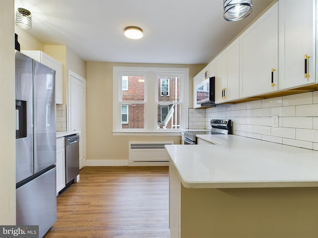 kitchen featuring kitchen peninsula, appliances with stainless steel finishes, decorative backsplash, white cabinets, and light hardwood / wood-style floors