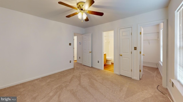 unfurnished bedroom with light carpet, a walk in closet, ensuite bath, ceiling fan, and a closet