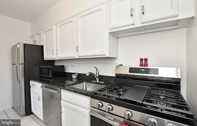 kitchen featuring sink, white cabinets, light tile patterned floors, dark stone countertops, and stainless steel appliances