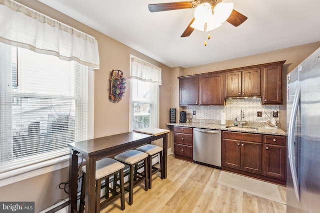 kitchen featuring light stone countertops, appliances with stainless steel finishes, tasteful backsplash, sink, and light hardwood / wood-style flooring