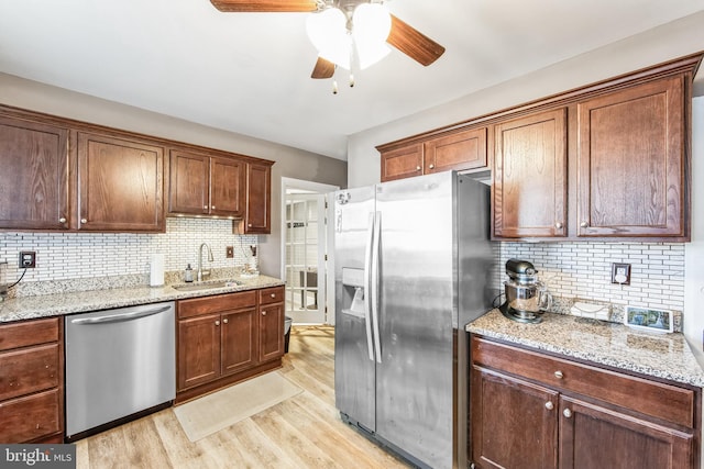 kitchen with decorative backsplash, light stone counters, stainless steel appliances, sink, and light hardwood / wood-style flooring