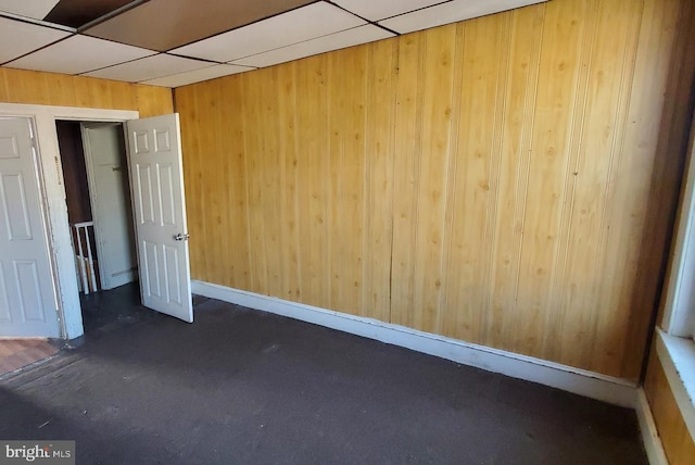 spare room featuring a drop ceiling and wooden walls