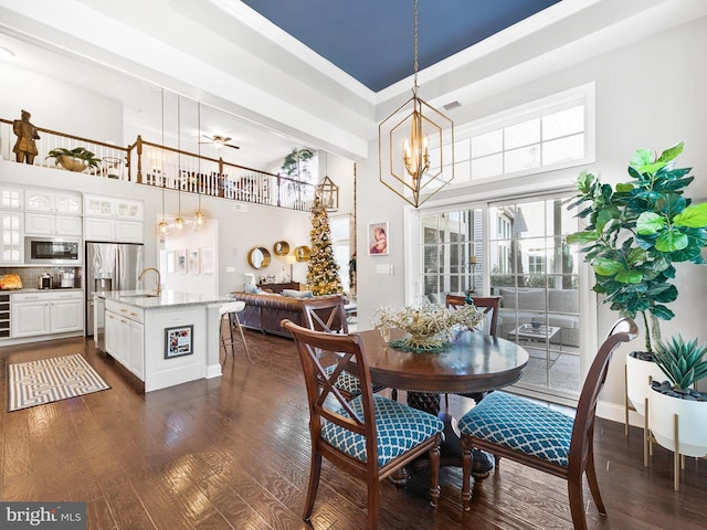 dining space featuring sink, dark hardwood / wood-style flooring, a towering ceiling, ceiling fan with notable chandelier, and ornamental molding