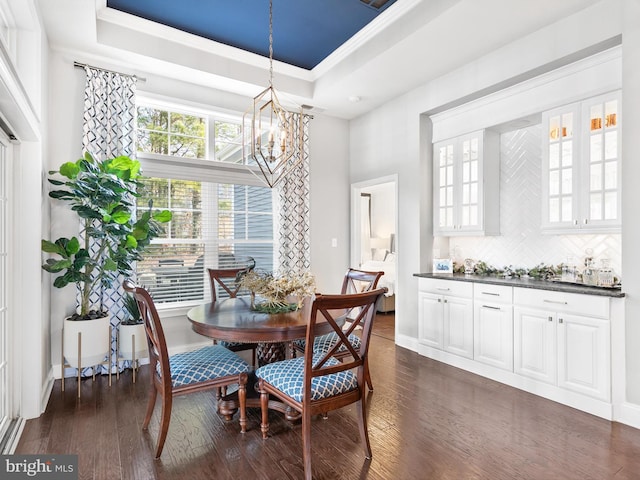 dining area featuring an inviting chandelier, a raised ceiling, and dark wood-type flooring