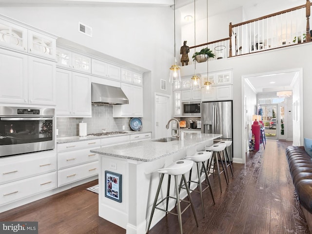 kitchen with wall chimney exhaust hood, white cabinetry, a towering ceiling, and appliances with stainless steel finishes