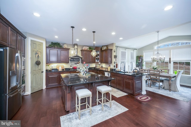 kitchen featuring wall chimney range hood, a kitchen island, stainless steel appliances, and decorative light fixtures