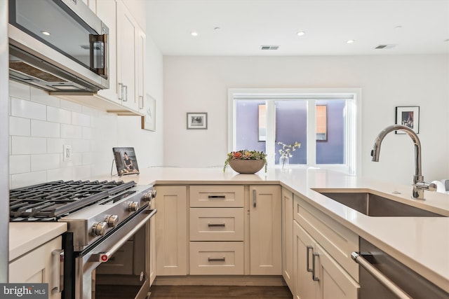 kitchen with sink, tasteful backsplash, dark hardwood / wood-style flooring, cream cabinets, and appliances with stainless steel finishes