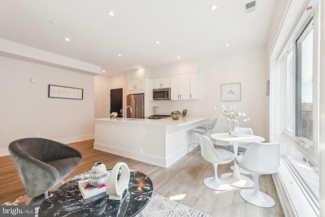 kitchen with white cabinetry, kitchen peninsula, light hardwood / wood-style floors, a breakfast bar area, and appliances with stainless steel finishes