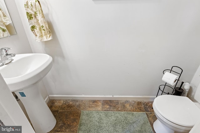 bathroom with toilet, stone finish flooring, baseboards, and a sink