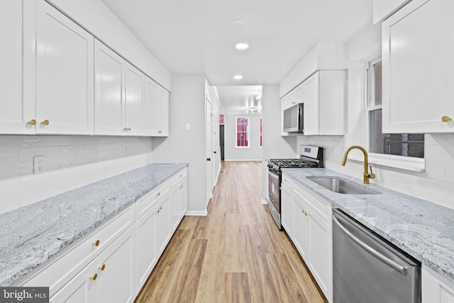 kitchen featuring light stone countertops, appliances with stainless steel finishes, sink, light hardwood / wood-style flooring, and white cabinetry