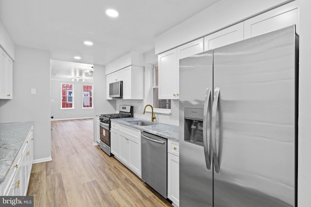 kitchen with white cabinets, sink, light hardwood / wood-style flooring, appliances with stainless steel finishes, and light stone counters