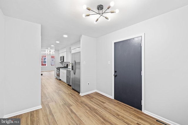 kitchen with a chandelier, white cabinets, light hardwood / wood-style floors, and appliances with stainless steel finishes