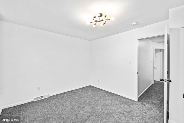 spare room with dark carpet and an inviting chandelier