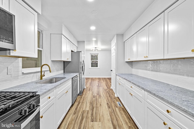 kitchen with light hardwood / wood-style floors, light stone counters, white cabinetry, and stainless steel appliances