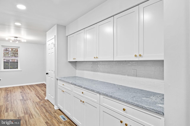 bar featuring backsplash, light hardwood / wood-style floors, white cabinetry, and light stone counters