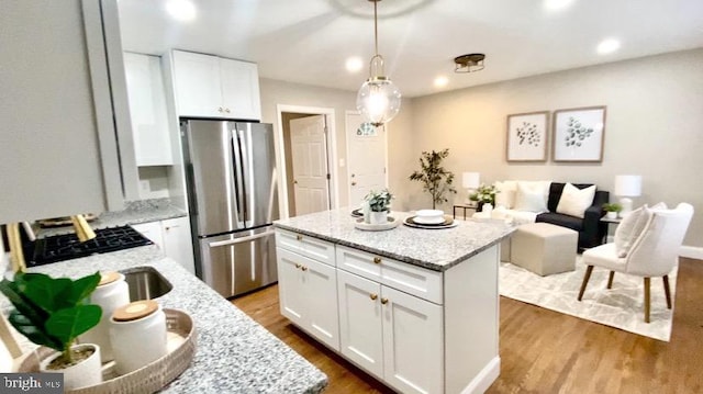 kitchen with stainless steel refrigerator, white cabinetry, a center island, and hanging light fixtures