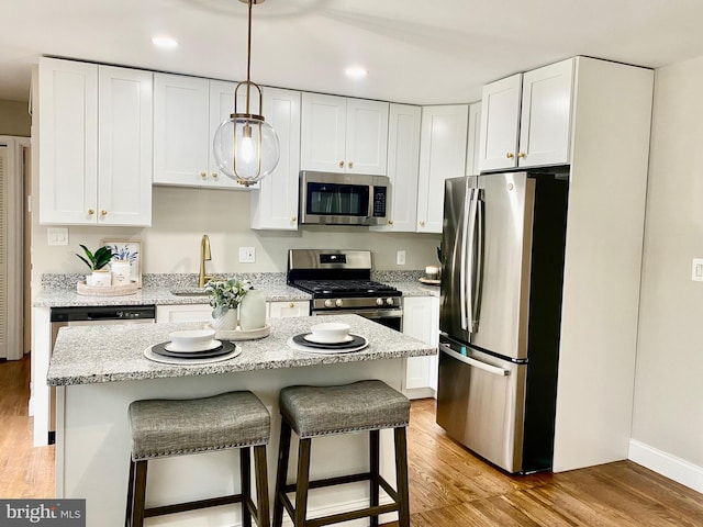 kitchen featuring a center island, white cabinets, hanging light fixtures, light wood-type flooring, and appliances with stainless steel finishes