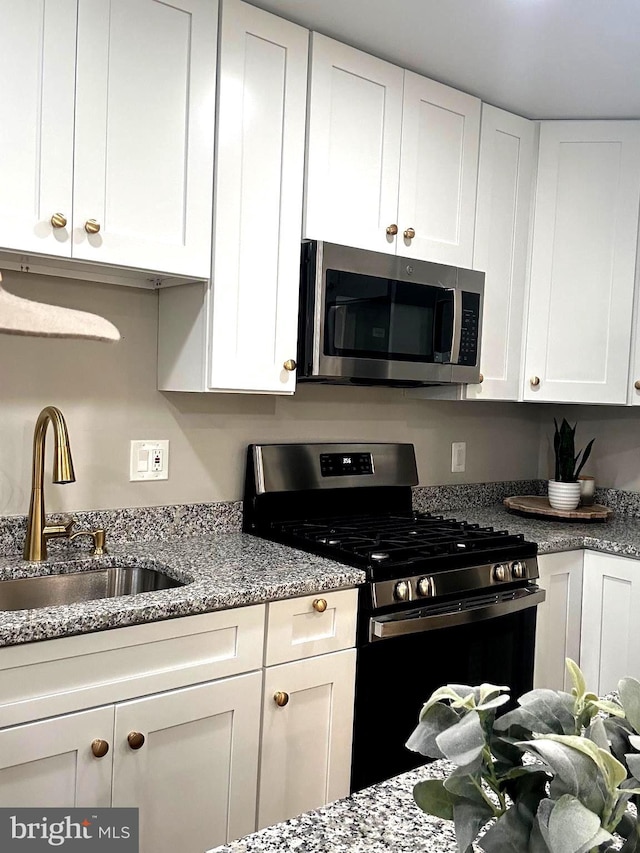 kitchen with white cabinets, stainless steel appliances, light stone countertops, and sink