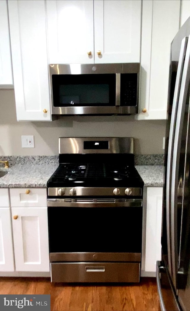 kitchen with white cabinets, light hardwood / wood-style floors, light stone countertops, and stainless steel appliances