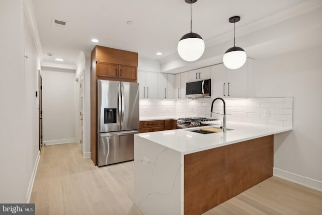 kitchen featuring kitchen peninsula, appliances with stainless steel finishes, sink, pendant lighting, and white cabinetry