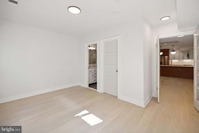 unfurnished bedroom featuring ensuite bathroom, light wood-type flooring, and stainless steel refrigerator with ice dispenser