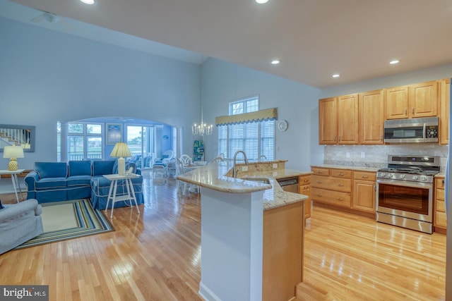 kitchen with sink, a kitchen island with sink, stainless steel appliances, a chandelier, and decorative backsplash