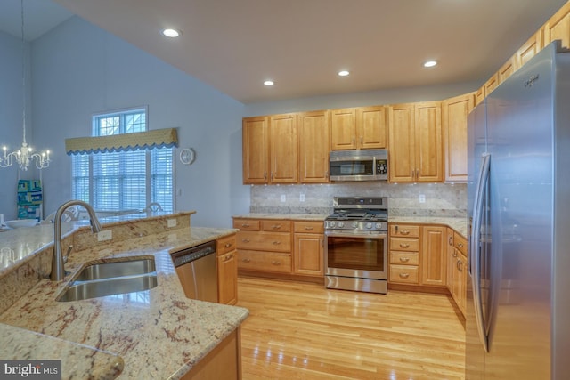 kitchen with decorative light fixtures, sink, light stone counters, and stainless steel appliances