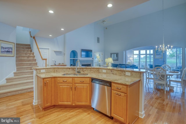 kitchen with a high ceiling, sink, stainless steel dishwasher, an island with sink, and light stone counters