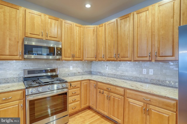 kitchen with tasteful backsplash, light stone countertops, stainless steel appliances, and light hardwood / wood-style floors