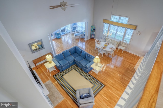 living room with ceiling fan, a towering ceiling, and wood-type flooring