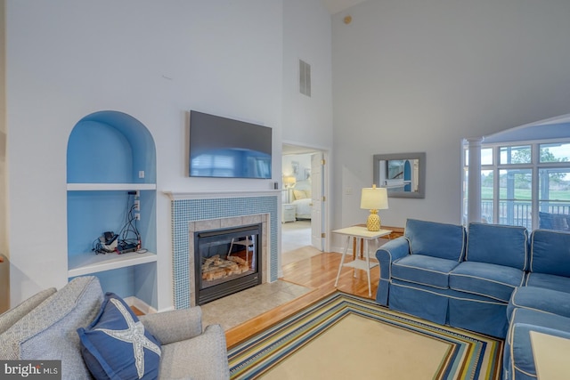 living room with decorative columns, built in shelves, hardwood / wood-style floors, and a tiled fireplace